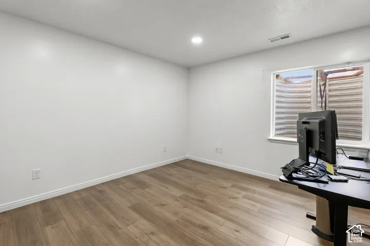 Bright, light-filled office space featuring pristine white walls, recessed ceiling lighting, and wood-finish flooring throughout