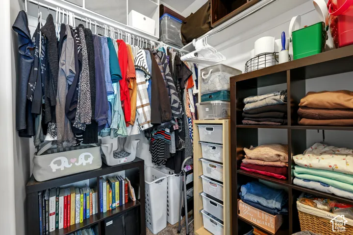 Organized walk-in closet featuring dual clothing rods with multiple hanging sections, wood-finish shelving with dedicated storage compartments, woven storage baskets, built-in drawer units, and a lower shelf system displaying neatly folded textiles and li