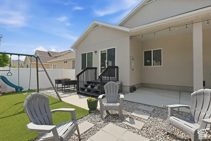 Manicured artificial turf area, concrete patio, white privacy fencing, raised garden beds, and exterior string lighting