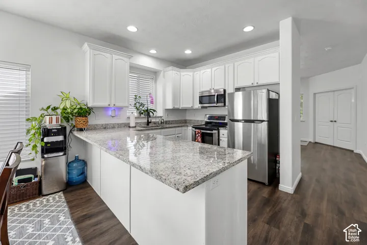 Modern kitchen featuring white cabinetry, stainless steel appliances, granite-style countertops with waterfall island edge, recessed ceiling lighting, and wood-finish flooring throughout the open-concept space