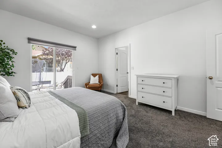 Bright secondary bedroom featuring dual beds, abundant natural light from sliding glass doors opening to a private balcony, carpeted flooring, white painted walls, a white dresser with multiple drawers, and direct access to an ensuite bathroom with glass-