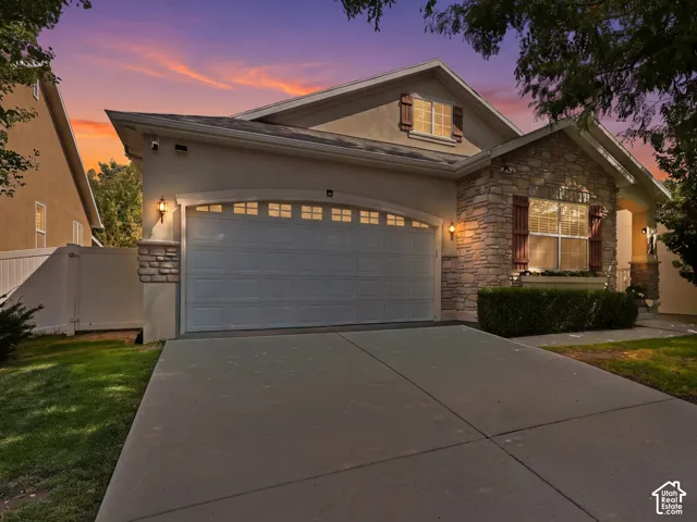 Stucco and stone exterior featuring a two-car garage, established front landscaping, and a covered porch entry
