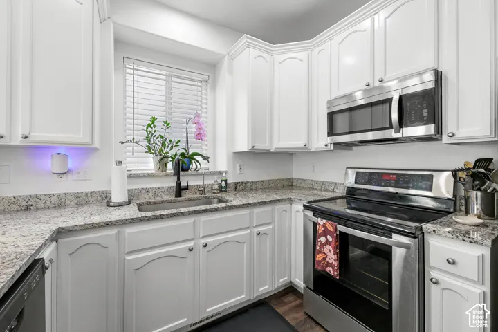 White cabinetry with silver-tone hardware, stainless steel appliances, speckled stone countertops, undermount sink with a matte black faucet, and wood-finish flooring