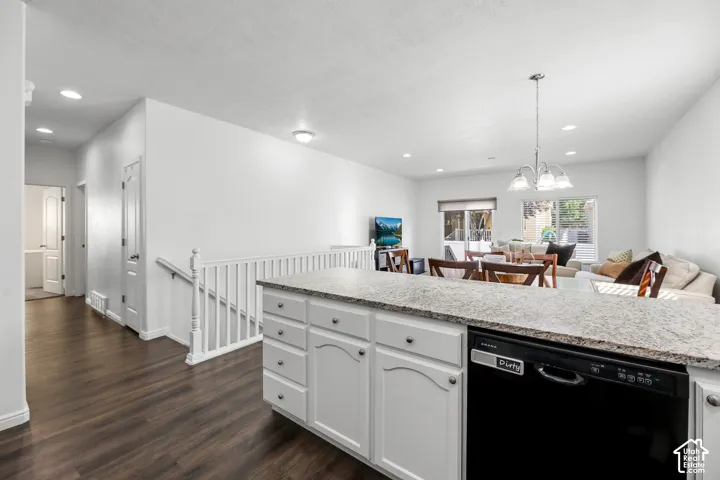 Open-concept kitchen and living area featuring white cabinetry with brushed hardware, quartz countertops, stainless steel appliances including a black dishwasher, wood-finish flooring throughout, recessed and pendant lighting, and a white railed staircase