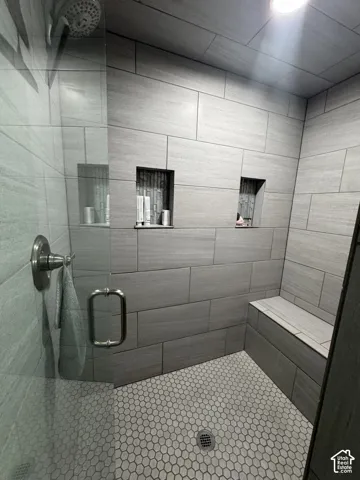 Spacious shower with large format tile walls, recessed shower niches, a built-in bench, and a hexagon-tiled floor