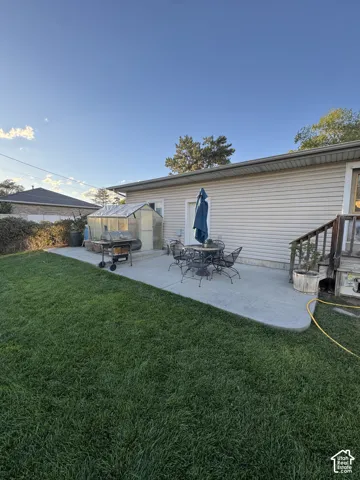 Expansive grassy yard with a concrete patio, a detached greenhouse, and wood deck with railings