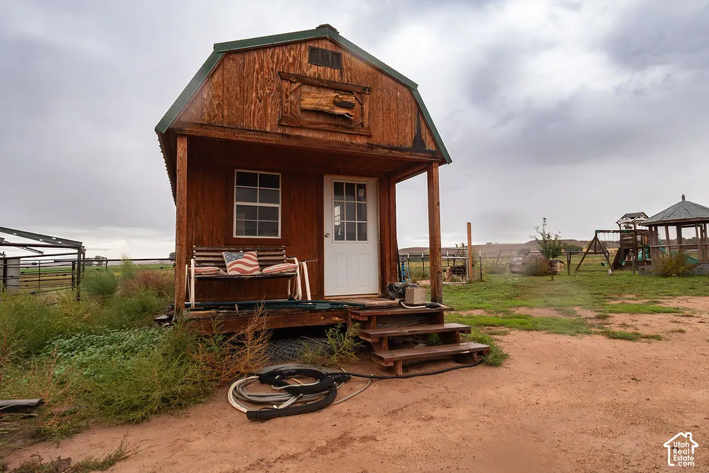 Wood-sided shed with a green metal roof, front porch, white entry door, and a single window and power.