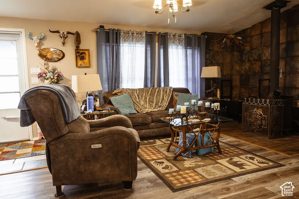 Living area featuring wood-finish flooring, a wood-burning stove with a metal screen, a floor-to-ceiling stone-tiled wall accent, and a five-light chandelier