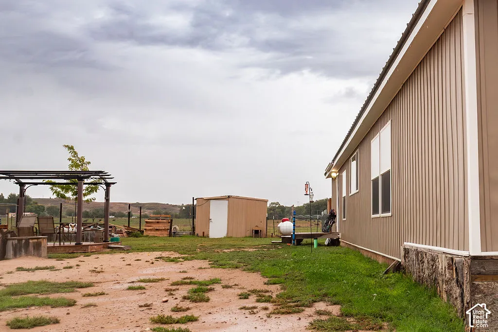 Exterior featuring a neutral-toned siding, white-trimmed windows, a metal roof, an outdoor pergola structure, and an ancillary shed