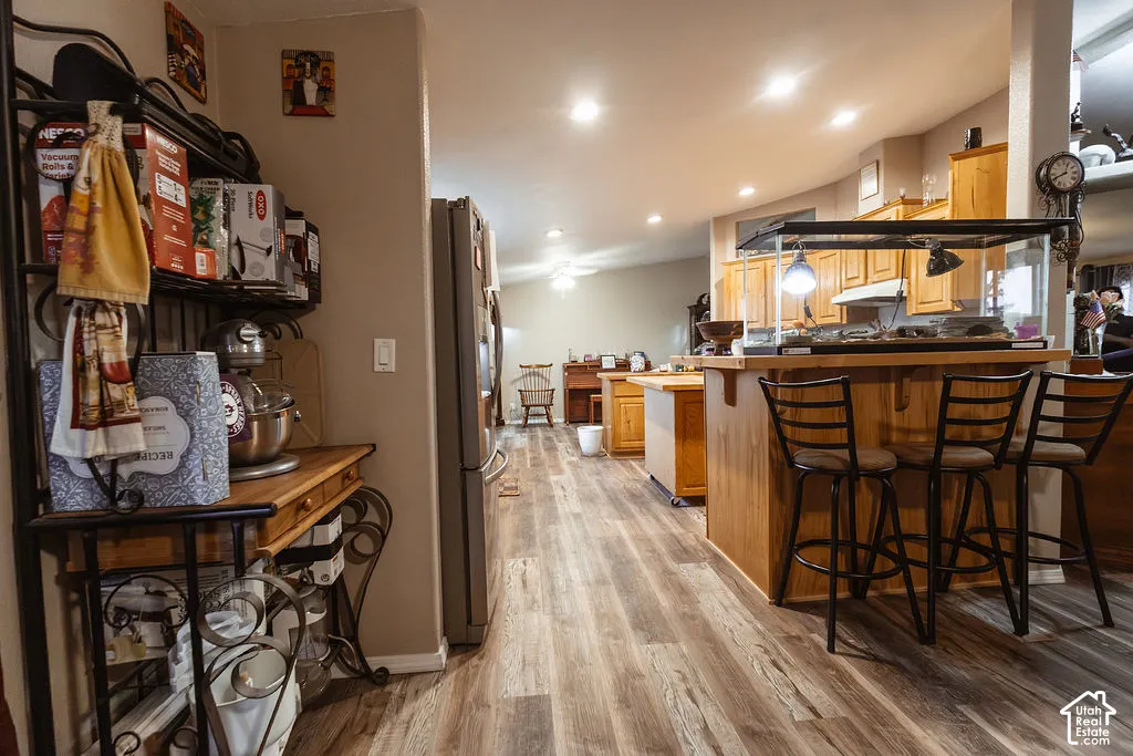 Wood-finish flooring throughout, light wood cabinetry, recessed lighting, and a kitchen island with bar seating
