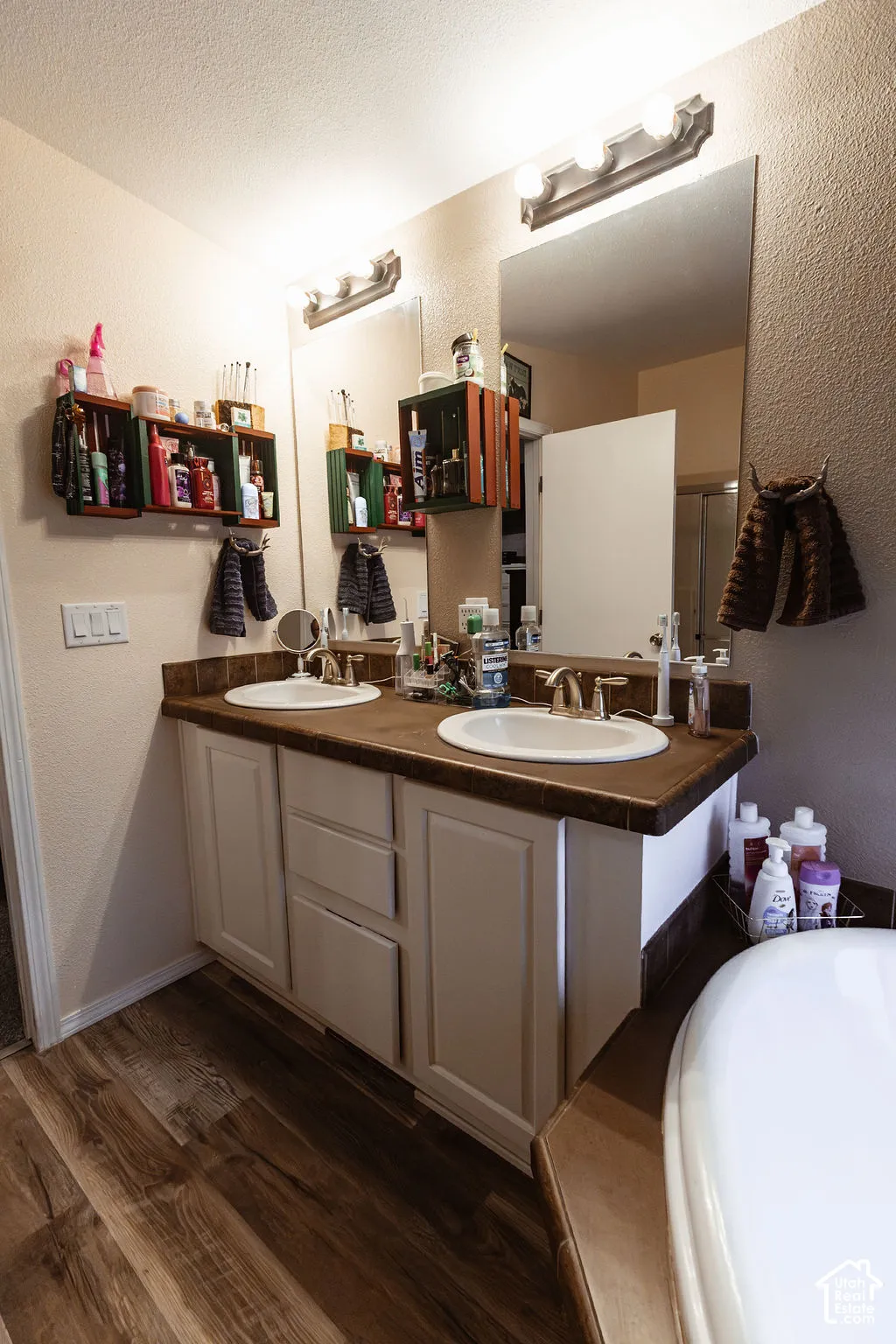 Dual vanity with white cabinetry, wood-finish flooring, and a large wall-mounted mirror