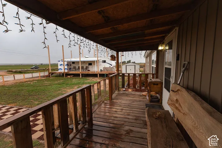 Covered front porch with wood-plank flooring, wood railing, and exterior wall lighting