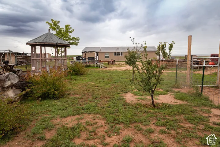 Expansive outdoor space featuring a gazebo with a shingled roof, a fenced area, and several young trees