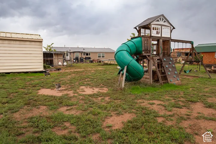 Exterior yard featuring a wood-structure play system with a slide, climbing wall, and swing set, accompanied by a detached metal-sided storage building