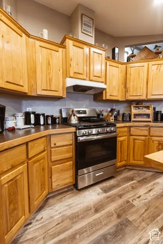 Natural finish wood cabinetry, stainless steel gas range, over-the-range microwave, dark countertops, and wood-finish flooring