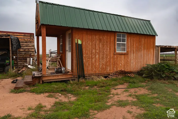 Wood-sided shed featuring a green metal gable roof, an elevated wood porch with steps, and a single-pane window