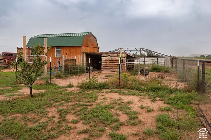 Wood-sided barn with a green metal roof, chain link fencing, and an open metal-framed structure