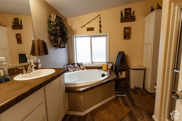 Built-in soaking tub with a frosted window, wood-finish flooring, white vanity with a single sink, and white built-in cabinetry
