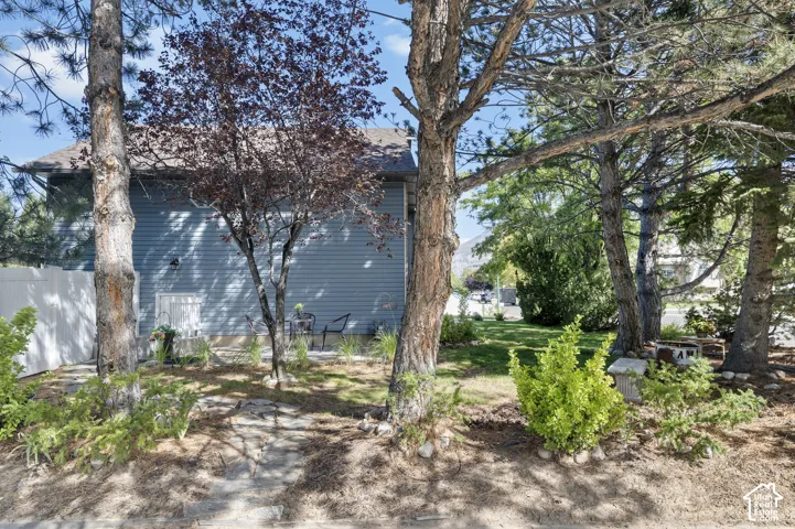 Side exterior with brand new siding, a white privacy fence, and mature trees, entrance to home to access daylight basement level and basement apartment