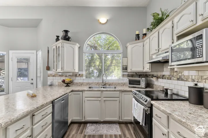 Kitchen with white cabinetry, light-toned countertops, a stainless steel dishwasher, two year old range and oven, and an arched window