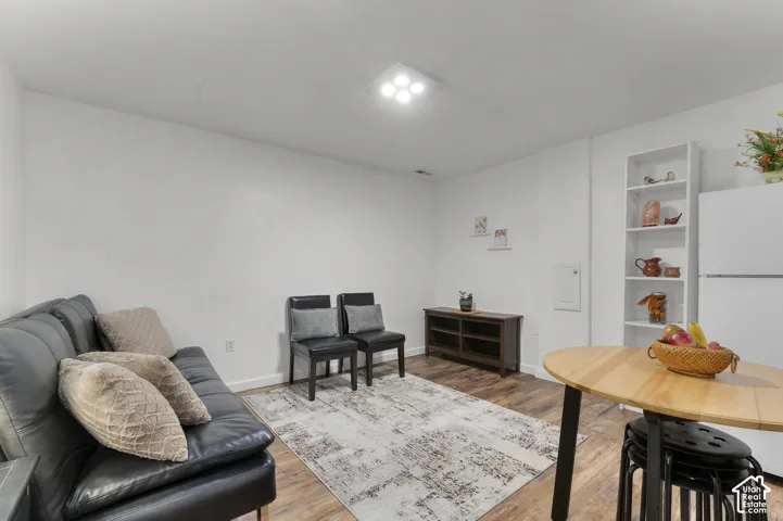 Wood-finish flooring, recessed ceiling lighting, built-in shelving, white refrigerator, and a light wood-finish table