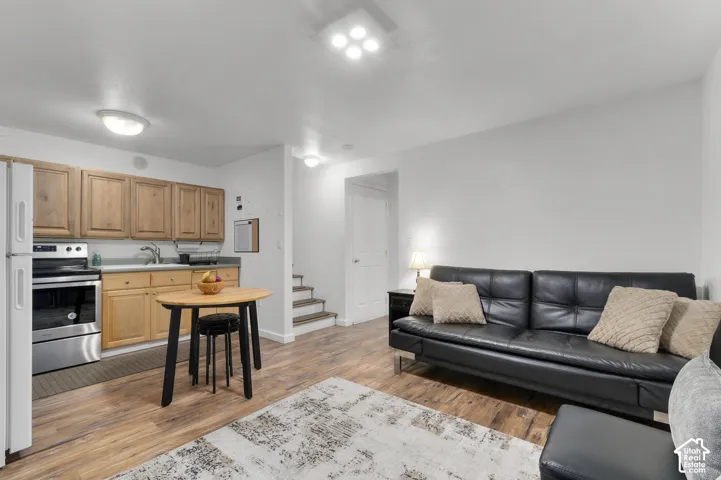 Open-concept living area featuring wood-finish flooring, a kitchen with natural wood cabinetry, stainless steel appliances, and ceiling-mounted lighting fixtures