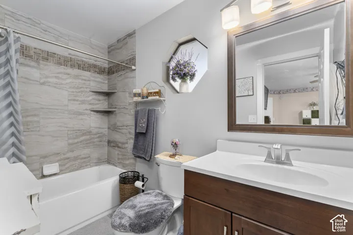 Master ensuite Tub/shower combination with tile surround and decorative accent band, built-in corner shelves, vanity with wood-finish cabinetry, integrated sink, and wall-mounted lighting fixture
