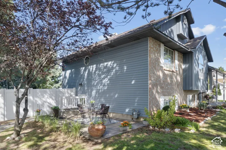 Exterior featuring a brick and brand new siding facade, private apartment patio area, white privacy fence, and manicured landscaping with mature trees