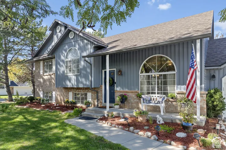 Multi-level exterior featuring brick and brand new vertical siding, arched window, and landscaped front yard with mature trees