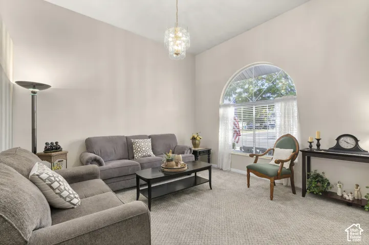 High ceiling with an attached decorative chandelier, arched window with horizontal blinds, and neutral wall tones