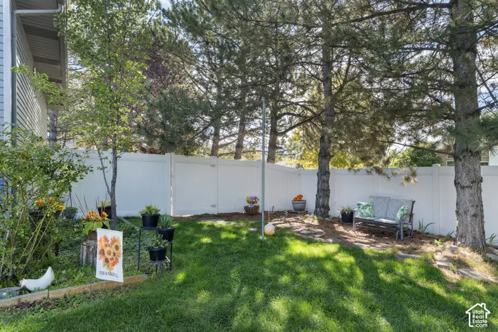 Expansive backyard featuring a manicured lawn, mature trees, and a white privacy fence, small sitting area
