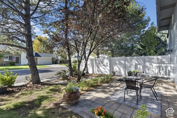 Paver patio area for basement apartment with a white privacy fence and mature trees,