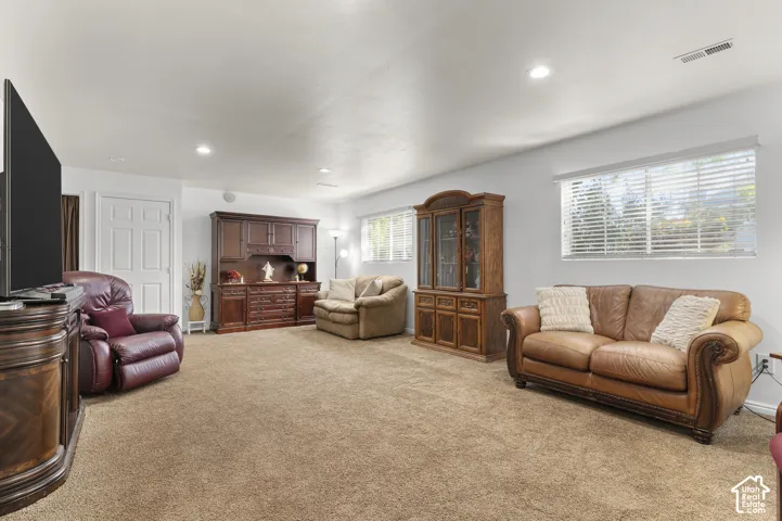 Recessed lighting illuminates the carpeted room, featuring white walls and multiple daylight windows