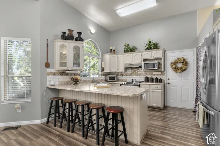 High ceiling kitchen featuring wood-finish flooring, white cabinetry, a kitchen island with beadboard detailing, and a subway tile backsplash