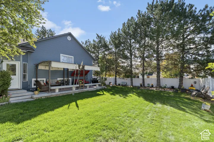 Expansive backyard lawn, privacy fencing, mature trees, and a covered Trex deck area with a pergola