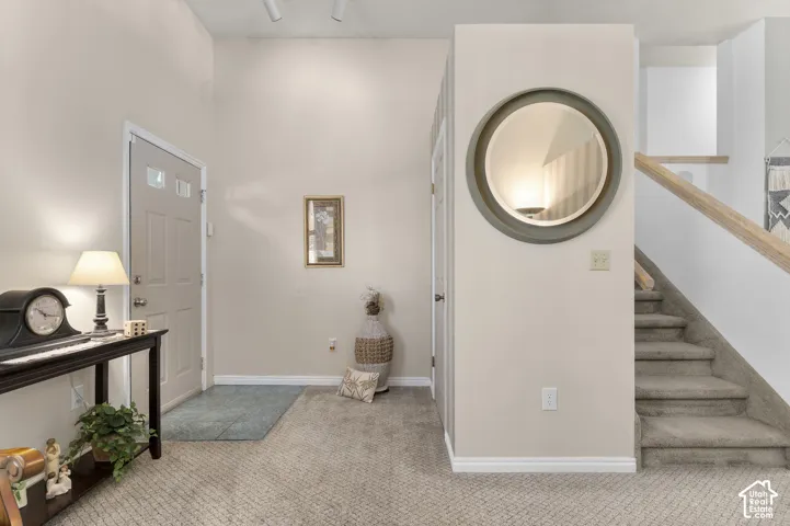 Entryway with a light-colored door featuring glass inserts, wall-to-wall carpeting, and a staircase with a wooden handrail