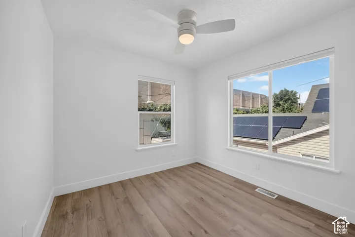 White walls, wood-finish flooring, two windows with white trim, and a ceiling fan with integrated lighting