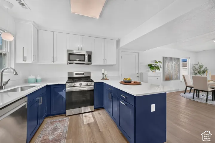 Contemporary kitchen featuring two-tone cabinetry, stainless steel appliances, white countertops, a stainless steel sink, and wood-finish flooring