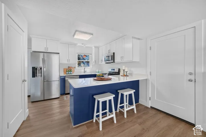 Kitchen featuring wood-finish flooring, white cabinetry, stainless steel appliances, and a central island with a contrasting blue base