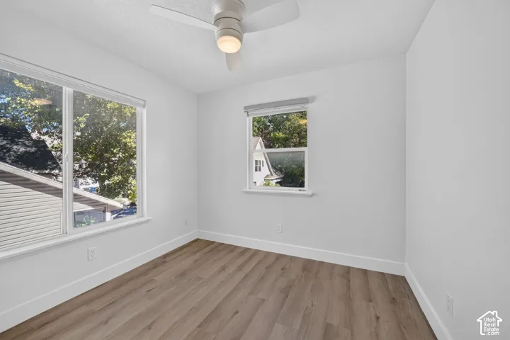 Wood-finish flooring, white walls, two windows with roller shades, and a ceiling fan with integrated lighting