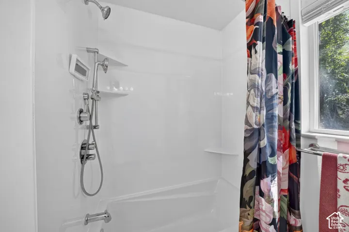 White tub and shower combination with chrome fixtures, a handheld showerhead, and integrated shelving