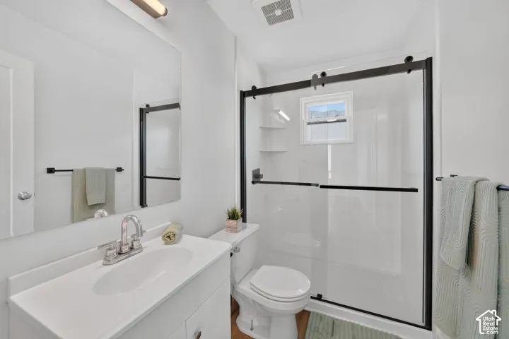 Bathroom featuring a white vanity with integrated sink, chrome faucet, large wall mirror, and a shower enclosure with black-framed sliding glass doors