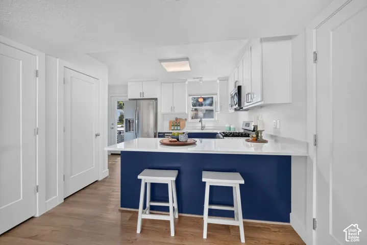 Kitchen featuring wood-finish flooring, white cabinetry, a blue kitchen island, and a stainless steel refrigerator