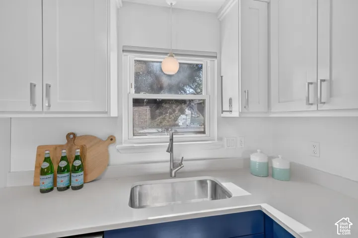 White shaker-style cabinetry, stainless steel sink, contemporary faucet, quartz countertops, and a modern pendant light