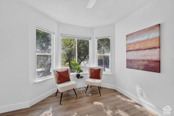 Bay window with multiple large glass panes, wood-finish flooring, white painted walls, and a ceiling-mounted fan