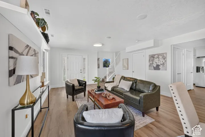 Light wood-finish flooring, white walls, recessed ceiling lighting, a white paneled entry door with sidelights, and a white staircase with a wooden handrail