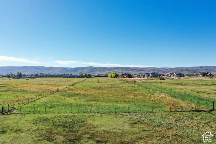 Expansive open field with partial fencing and distant residential structures