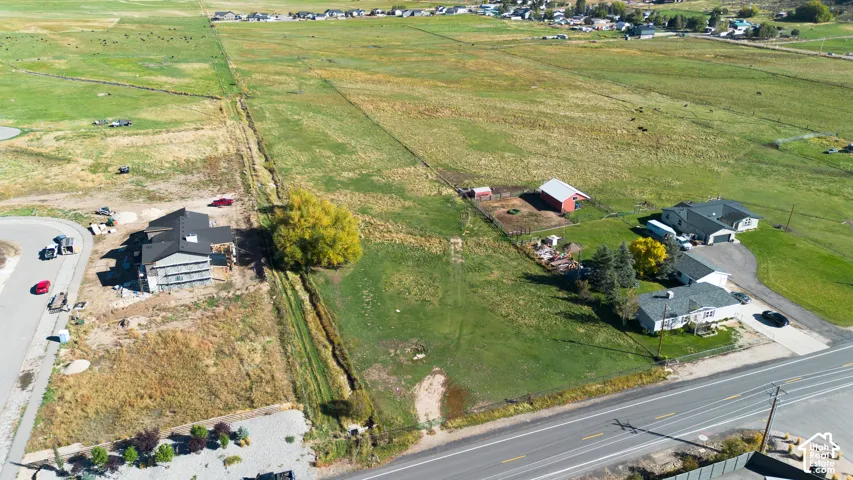 Expansive open land featuring a paved road frontage, established residential structures, and distant community elements