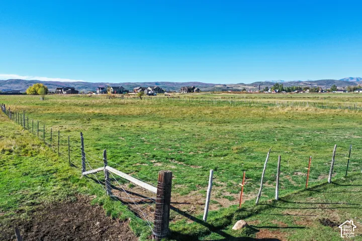 Expansive green field with a partial wire fence and distant structures