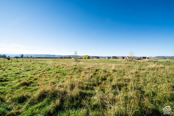 Expansive grass and brush land, featuring wood post fencing, and distant residential structures